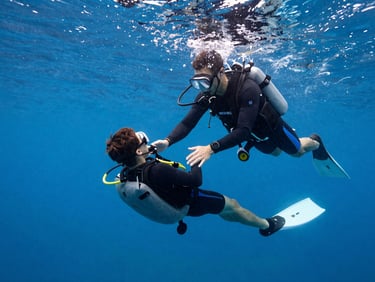 Diving instructor guiding a student underwater, both in perfect trim, clear blue water, demonstrating safety skills.
