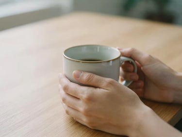 Close-up of hands holding a warm ceramic mug on a clean wooden desk, soft diffused natural daylight, calming muted tones, shallow depth of field