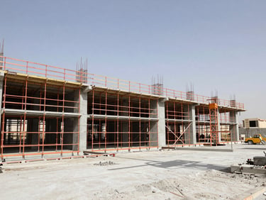 Wide-angle industrial shot of an active concrete construction site in Riyadh, harsh direct sunlight, safety orange scaffolding, sharp focus, 35mm lens.