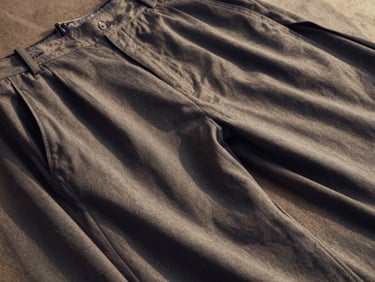High-angle shot of men's tailored grey trousers, fabric draping visible, architectural shadows, editorial framing, focus on movement.