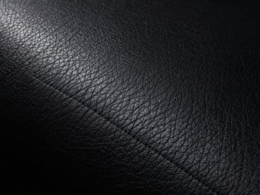 Macro close-up studio shot of rich black genuine automotive leather grain, sharp highlights, deep shadows, emphasizing texture, moody lighting, 50mm