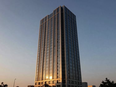 Modern steel and glass office tower in Gurgaon at sunset, dramatic late-afternoon sun casting long shadows, sharp architectural lines