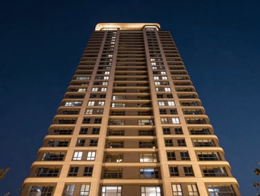 Wide-angle symmetrical exterior shot of a modern luxury residential tower at twilight, warm champagne lighting, deep navy sky background, premium architectural photography.