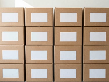 Neat stack of cardboard shipping boxes with clean labels on a concrete floor, bright indirect sunlight