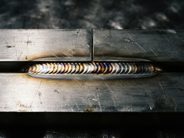 Macro shot of a flawless TIG weld joint on brushed stainless steel, dramatic side lighting, industrial editorial style, 35mm lens