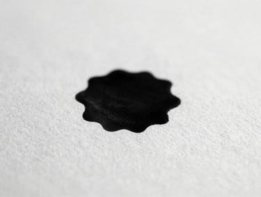 Close-up of ink spreading on textured paper, soft diffused daylight, high-contrast black and white, shallow depth of field, 35mm film grain, minimalist editorial photography