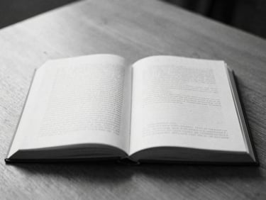 Open book with a minimalist design on a wooden table, soft diffused daylight, high-contrast black and white, shallow depth of field, 35mm film grain, minimalist editorial photography