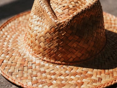 Close-up of a hand-woven palm hat, intricate weave visible, harsh natural sunlight casting deep shadows, warm editorial photography, rich terracotta tones, 35mm film