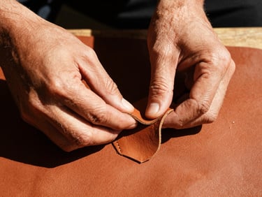 Close-up of hands working with tanned leather, shaping a huarache, harsh natural sunlight, deep shadows highlighting texture, warm editorial photography.