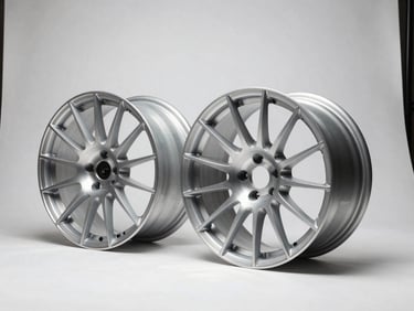 Three-quarter profile studio shot of two forged aluminum wheels side by side on a stark white ground, hard controlled strobe light from the right casting sharp spoke shadows, one wheel slightly closer showing spoke detail evolution between model generations, no car context, overhead grid framing