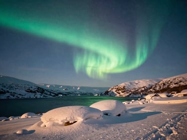 Wide shot of a snow-covered fjord under a vibrant aurora borealis, low horizon, deep blue and green tones, atmospheric winter photography.