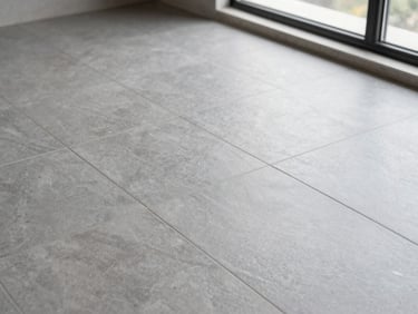 Overhead close-up of freshly laid large-format grey porcelain floor tiles with tight grout lines, natural daylight from a wide window casting soft shadows, sharp detail on the tile surface texture