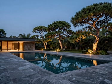 Twilight architectural shot of a minimalist zero-edge pool reflecting a deep blue sky, slate gray stone decking, warm uplighting on architectural pines