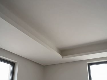 Architectural detail shot of a completed false ceiling with recessed lighting channels, clean gypsum board seams and shadow-line joints visible under diffused daylight from a side window, empty room below showing ceiling scale