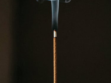 Close-up of an incense stick showing natural texture, with a thin wisp of white smoke against a dark background, 35mm film grain.