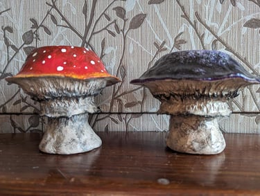 Hand-painted red amanita and purple clay mushroom figurines on a wooden shelf.