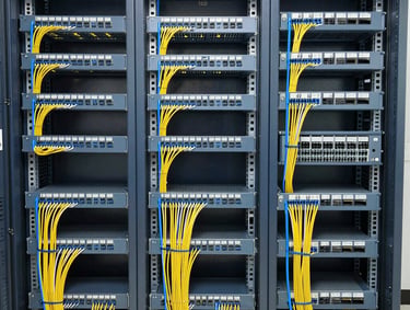 Wide environmental shot of a structured enterprise network closet, patch panels fully populated with colour-coded cables running in neat horizontal trays, rack-mounted switches with organised cable bundles, bright even overhead lighting showing clean termination standards and labelling throughout, framed to capture full rack height and cable pathway
