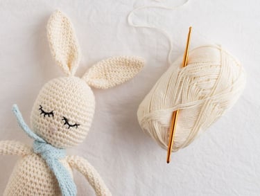 Amigurumi de crochet en forma de conejo color beige con madeja de estambre y gancho