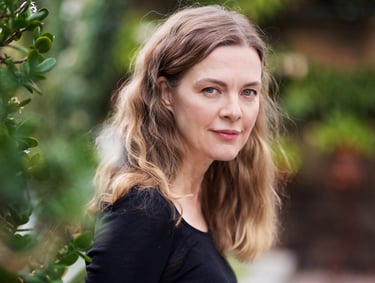 A beautiful middle-aged woman with long curly hair and a black shirt standing in a garden and looking at the camera