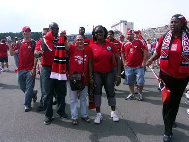 Crowd of Soca Warriors fans wearing red jerseys and waving flags at an event.