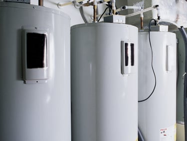 Three large commercial water heater tanks installed in a row with copper pipes.