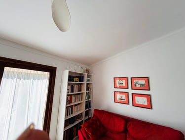 Living room with a red sofa, white bookshelf, and framed artwork on white walls.