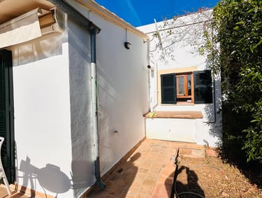 White stucco Mediterranean house patio with terracotta tile walkway and black window shutters.