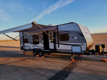 Jayco Jay Flight travel trailer with extended awning parked at a campsite during sunset.