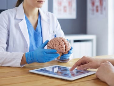 Close-up of a neurology provider holding a brain model and using a tablet to explain diagnosis and lifestyle factors to a pat