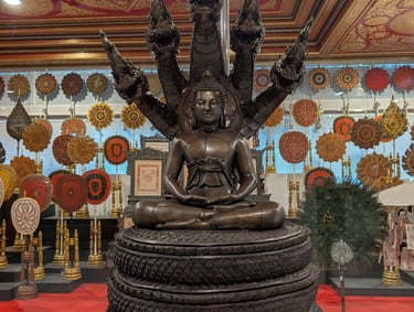 Bronze meditating Buddha statue sheltered by a seven-headed Naga serpent at a Thai temple.