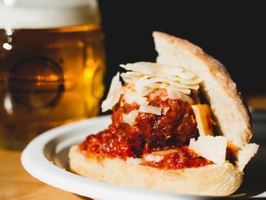 Meatball with marinara on a dinner roll with parmesan cheese shredded on top.