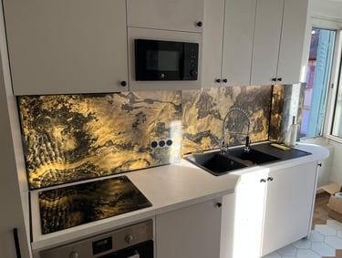 Modern white kitchen featuring a backlit gold and black marble effect glass backsplash and black sink.
