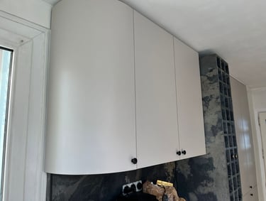 Modern white curved kitchen wall cabinets with black knobs next to a dark stone wine rack.