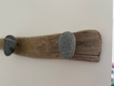 Handmade wall-mounted coat rack featuring smooth river stones on a rustic driftwood base.