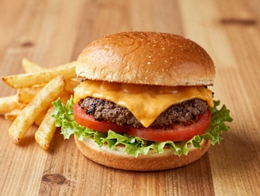 Bright food photography of a gourmet cheeseburger with melting cheddar, crisp lettuce, and fresh tomatoes, served with golden french fries on a warm wood table