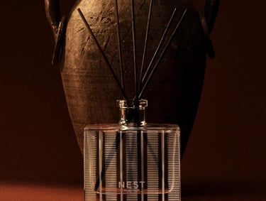 NEST New York glass reed diffuser set in front of a rustic antique clay amphora vase.