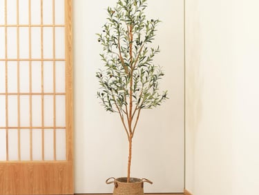 Tall artificial olive tree in a woven seagrass basket planter against a white wall and shoji screen.