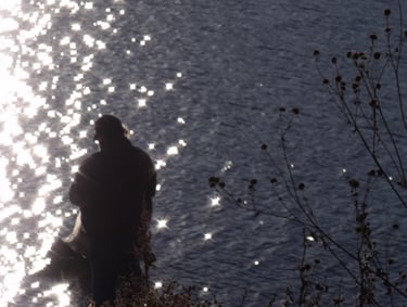 a shadow of a man standing in front of a sparkling lake