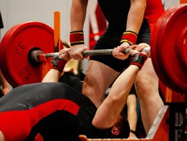 A powerlifter performs a heavy bench press with a spotter during a weightlifting competition.