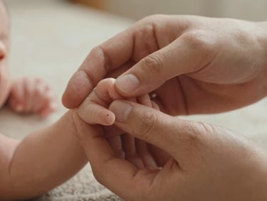A close-up of a family's hands intertwined, showing a newborn's tiny fingers. Soft cocoa and warm sand color palette. Natural, intimate lighting in a light and airy North American / US (West Michigan) home setting.