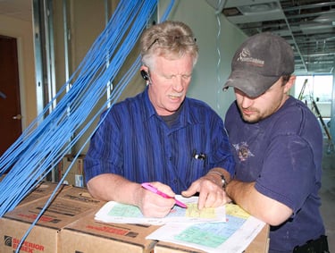 Technicians review a cabling project design plan at a professional network installation site.