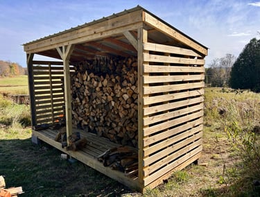 a wooden storage shed with logs stacked on top of it