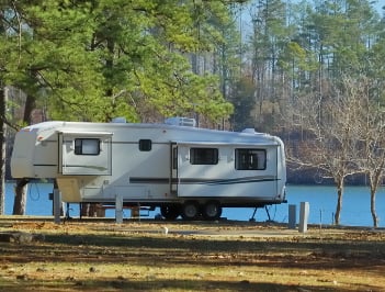 a camper trailer parked on the shore of a lake