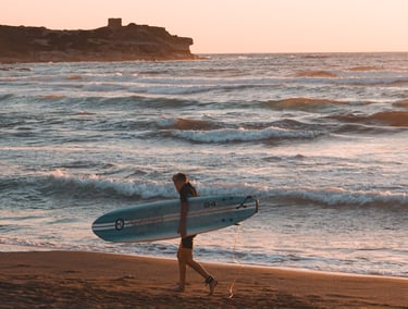 Surfer at sunset on Porto Ferro beach, Sassari, Sardinia, one of the island’s top surf spots.