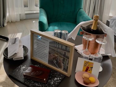 a table with a bottle of champagne, card, cake, macaroons, dessert, and framed letter