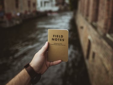 Journal titled "Field Notes" held up in front of a Canal; Photo by Vadim Sadovski on Unsplash 