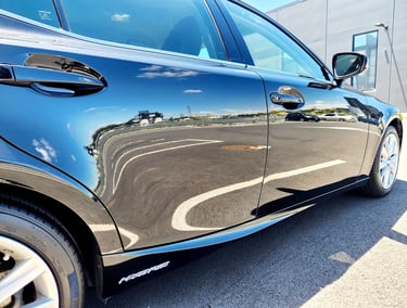Side view of a ceramic coated black sedan with a high-gloss finish reflecting the parking lot.