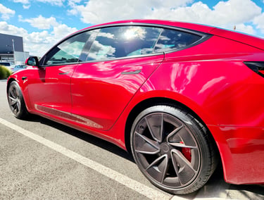 Side profile of a red Tesla Model 3 electric car parked under a sunny sky with graphene coating