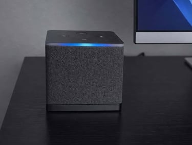 Amazon fire tv cube with fabric finish on a desk beside a computer monitor