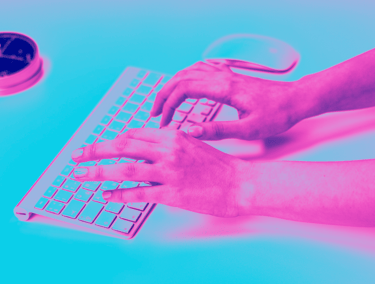 Hands typing on a wireless computer keyboard under vibrant pink and blue neon lighting.